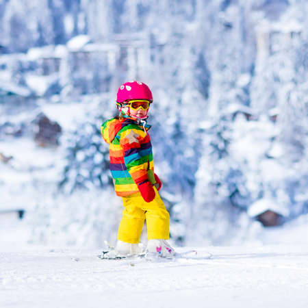 Child skiing in mountains. Active toddler kid with safety helmet, goggles and poles. Ski race for young children. Winter sport for family. Kids ski lesson in alpine school. Little skier racing in snowの写真素材