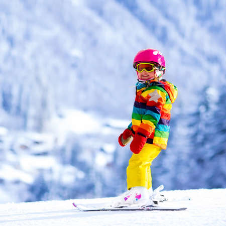 Child skiing in mountains. Active toddler kid with safety helmet, goggles and poles. Ski race for young children. Winter sport for family. Kids ski lesson in alpine school. Little skier racing in snowの写真素材