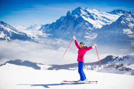Young active woman skiing in mountains. Female skier kid with safety helmet, goggles and poles enjoying sunny winter day in Swiss Alps. Ski race for adults. Winter and snow sport in alpine resort.の写真素材