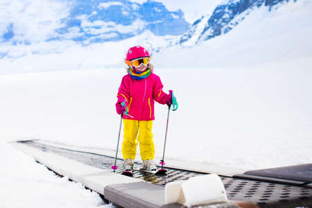 Child on magic carpet ski lift going uphill in the mountains on snowy winter day. Kids in winter sport school in alpine resort. Family fun in the snow. Little skier learning and exercising on a slope.の写真素材