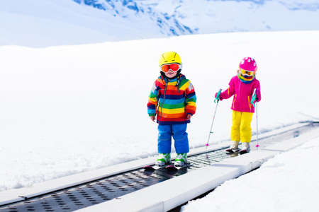 Children on magic carpet ski lift going uphill in the mountains on snowy winter day. Kids in winter sport school in alpine resort. Family fun in the snow. Little skier exercising on a slope.の写真素材