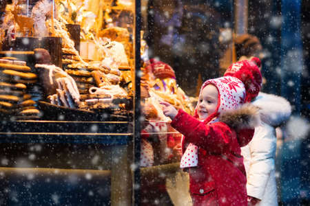 Children window shopping on traditional Christmas market in Germany on snowy winter day. Kids buying candy, pastry and gingerbread in confectionery. Boy and girl choosing sweets in Xmas bakery.の写真素材