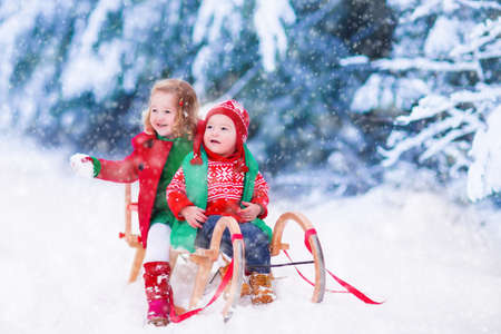Little girl and boy enjoy a sleigh ride. Child sledding. Toddler kid riding a sledge. Children play outdoors in snow. Kids sled in Alps mountains in winter. Outdoor fun for family Christmas vacation.の写真素材