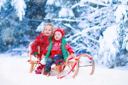 Little girl and boy enjoy a sleigh ride. Child sledding. Toddler kid riding a sledge. Children play outdoors in snow. Kids sled in Alps mountains in winter. Outdoor fun for family Christmas vacation.の写真素材