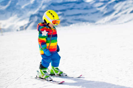 Child skiing in mountains. Active toddler kid with safety helmet, goggles and poles. Ski race for young children. Winter sport for family. Kids ski lesson in alpine school. Little skier racing in snowの写真素材
