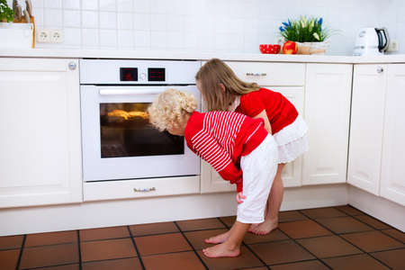 Little boy and girl, brother and sister baking delicious apple pie in white kitchen. Kids looking at fruit cake in the oven. Children bake at home. Toddler child and preschooler waiting for pastry.の写真素材