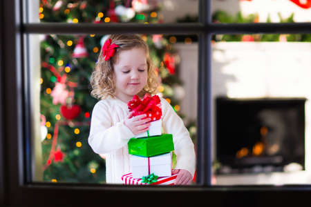 Family on Christmas morning at fireplace. Kids opening Xmas presents. Children under Christmas tree with gift boxes. Decorated living room with traditional fire place. Cozy warm winter day at home.の写真素材