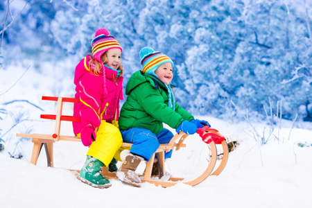 Little girl and boy enjoy a sleigh ride. Child sledding. Toddler kid riding a sledge. Children play outdoors in snow. Kids sled in Alps mountains in winter. Outdoor fun for family Christmas vacation.の写真素材
