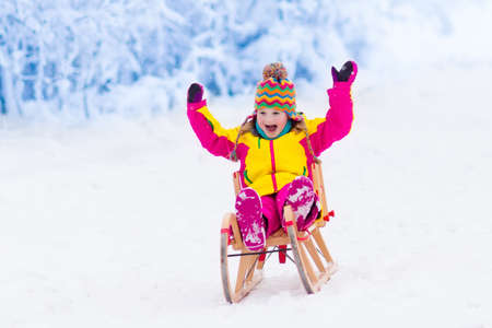 Little girl enjoying a sleigh ride. Child sledding. Toddler kid riding a sledge. Children play...