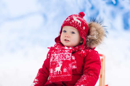 Little girl enjoying a sleigh ride. Child sledding. Toddler kid riding a sledge. Children play outdoors in snow. Kids sled in the Alps mountains in winter. Outdoor fun for family Christmas vacation.の写真素材