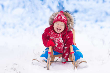 Little girl enjoying a sleigh ride. Child sledding. Toddler kid riding a sledge. Children play outdoors in snow. Kids sled in the Alps mountains in winter. Outdoor fun for family Christmas vacation.の写真素材