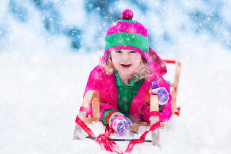 Little girl enjoying a sleigh ride. Child sledding. Toddler kid riding a sledge. Children play outdoors in snow. Kids sled in the Alps mountains in winter. Outdoor fun for family Christmas vacation.の写真素材