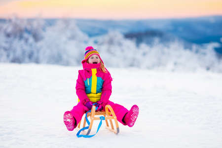 Little girl enjoying a sleigh ride. Child sledding. Toddler kid riding a sledge. Children play outdoors in snow. Kids sled in the Alps mountains in winter. Outdoor fun for family Christmas vacation.の写真素材