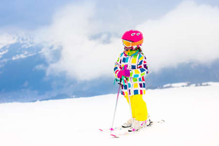 Child skiing in mountains. Active toddler kid with safety helmet, goggles and poles. Ski race for young children. Winter sport for family. Kids ski lesson in alpine school. Little skier racing in snowの写真素材