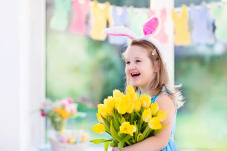 Happy little girl in bunny ears holding tulip flower bouquet. Kids celebrate Easter. Children having...