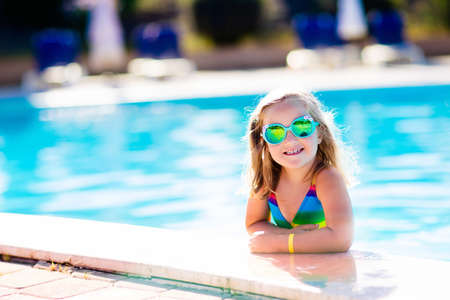 little girl playing in outdoor swimming pool jumping into water on summer vacation on tropical beach island child learning to swim in outdoor pool of luxury resort water toy and sunglasses for kidsの写真素材