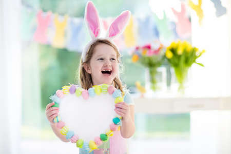 happy little girl in bunny ears holding a heart board with colorful easter eggs kids celebrate...