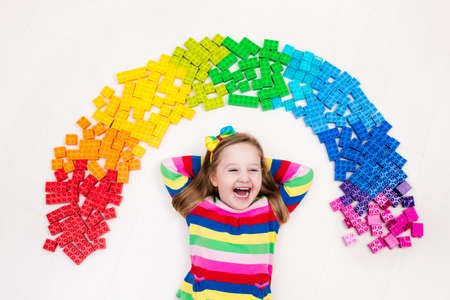 Funny little girl playing with colorful rainbow plastic blocks. Kids play, create and learn colors. Educational toys for creative children. Preschooler building block toys. Kid playing on the floor.の写真素材