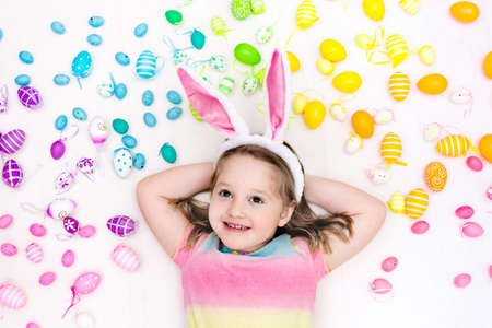 Funny little girl with bunny ears having fun on Easter egg hunt. Child playing with colorful Easter...