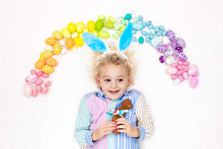 Funny little boy with bunny ears having fun on Easter egg hunt. Child playing with colorful Easter eggs. Kids play with pastel color rainbow eggs. Spring and Easter art and crafts for children.の写真素材