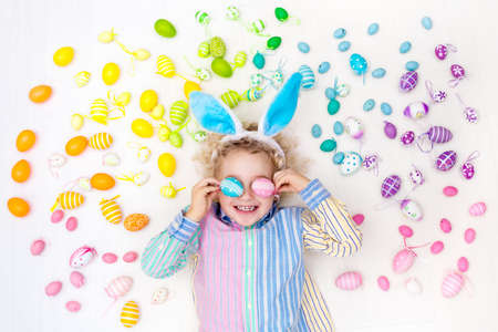 Funny little boy with bunny ears having fun on Easter egg hunt. Child playing with colorful Easter...
