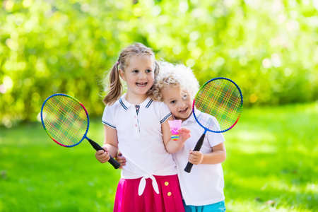 Active preschool girl and boy playing badminton in outdoor court in summer. Kids play tennis. School sports for children. Racquet and shuttlecock sport for child athlete. Kid with racket and shuttle.の写真素材