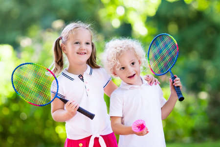 Active preschool girl and boy playing badminton in outdoor court in summer. Kids play tennis. School sports for children. Racquet and shuttlecock sport for child athlete. Kid with racket and shuttle.の写真素材