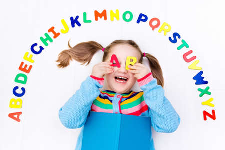 Happy preschool child learning to read and write playing with colorful roman alphabet letters. Educational abc toys and books for kids. School student doing homework. Kid reading in kindergarten.の写真素材