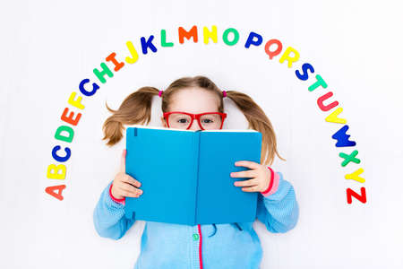 Happy preschool child learning to read and write playing with colorful roman alphabet letters. Educational abc toys and books for kids. School student doing homework. Kid reading in kindergarten.の写真素材