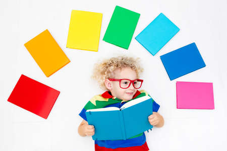 Little boy with colorful rainbow books. Happy back to school student. Child reading and doing homework. Preschooler kids learn and read a book. Curly funny kid in elementary school or kindergarten.の写真素材