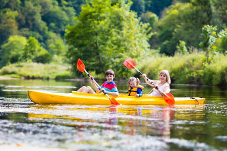 Happy family with two kids enjoying kayak ride on beautiful river. Mother with little girl and teenager boy kayaking on hot summer day. Water sport fun. Canoe and boat for children.の写真素材