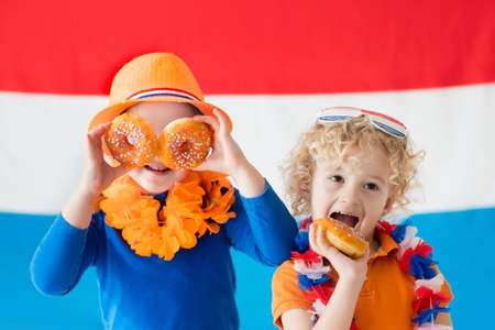 Little Dutch boy and girl wearing country symbols eating orange donuts celebrating King day. Children support Holland sport team. Kids from the Netherlands. Young sport fans with national flag.の写真素材