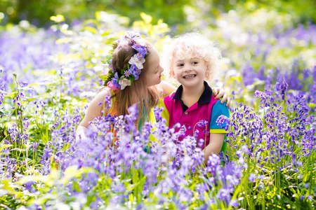 Kids with bluebell flowers, garden tools and wheelbarrow. Boy and girl gardening. Children play outdoor in bluebells, work, plant and water blue bell flower bed. Family fun in summer forest.の写真素材