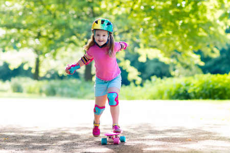 Child riding skateboard in summer park. Little girl learning to ride skate board. Active outdoor sport for school and kindergarten kids. Children skateboarding. Preschooler on longboard. Kid skating.の写真素材