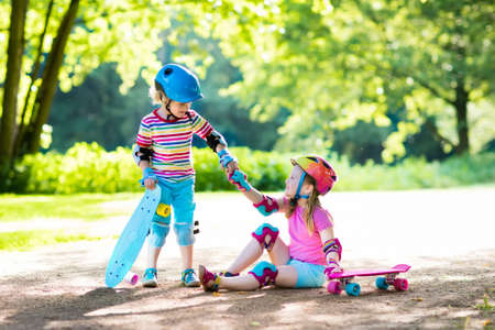 Children riding skateboard in summer park. Little girl and boy learn to ride skate board, help and support each other. Active outdoor sport for kids. Child skateboarding. Preschooler kid skating.の写真素材