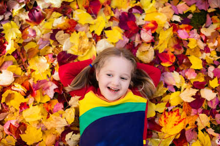 Kids play in autumn park. Children throwing yellow and red leaves. Little girl with oak and maple leaf. Fall foliage. Family outdoor fun in autumn. Toddler kid or preschooler child in fall.の写真素材