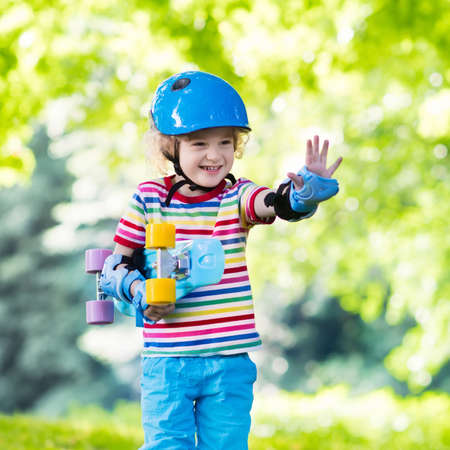 Child riding skateboard in summer park. Little boy learning to ride skate board. Active outdoor...