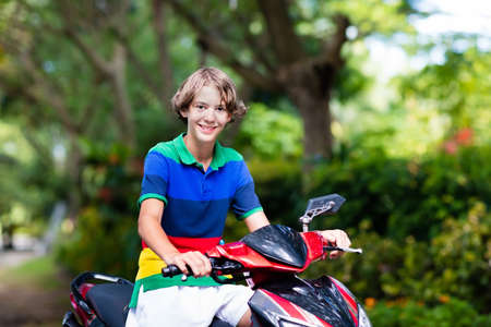 Teenager riding scooter. Teenage boy fun on motorbike ride on his way to school. Student on motorcycle in tropical city. Transportation and travel for young adult. Tourist exploring town by bike.の写真素材