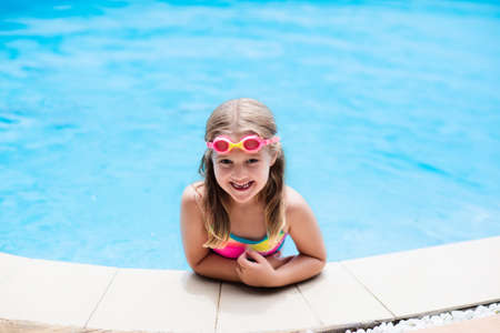 Child with goggles in swimming pool. Little girl learning to swim and dive in outdoor pool of tropical resort. Swimming with kids. Healthy sport activity for children. Sun protection. Water fun.の写真素材