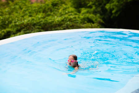 Child with goggles in swimming pool. Little girl learning to swim and dive in outdoor pool of tropical resort. Swimming with kids. Healthy sport activity for children. Sun protection. Water fun.の写真素材