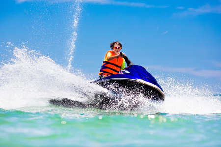 Teen age boy skiing on water scooter. Young man on personal watercraft in tropical sea. Active summer vacation for school child. Sport and ocean activity on beach holiday.の写真素材