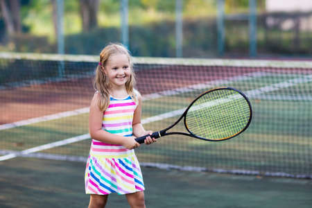 Child playing tennis on outdoor court. Little girl with tennis racket and ball in sport club. Active exercise for kids. Summer activities for children. Training for young kid. Child learning to play.の写真素材