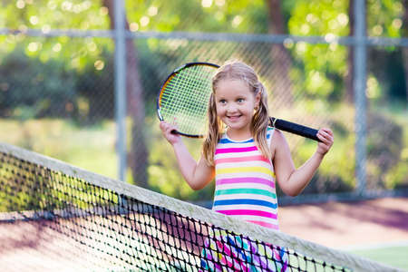 Child playing tennis on outdoor court. Little girl with tennis racket and ball in sport club. Active exercise for kids. Summer activities for children. Training for young kid. Child learning to play.の写真素材