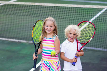 Boy and girl playing tennis on outdoor court. Kids with tennis racket and ball in sport club. Active exercise. Summer activities for children. Training for young kid. Child learning to play.の写真素材