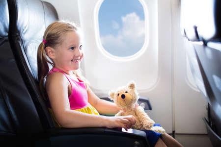 Child in airplane. Kid in air plane sitting in window seat. Flight entertainment for kids. Traveling with young children. Kids fly and travel. Family summer vacation. Girl with toy in airplane.の写真素材