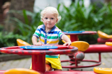 Kids on playground. Children play in summer park. Child on slide and swing on sunny day. Preschool or kindergarten yard. Daycare for young kid. Baby on play ground. Outdoor fun.の写真素材