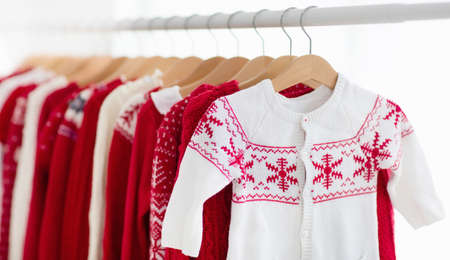 Clothes rack with red Christmas knit wear. Wardrobe with knitted winter jumper and dress. Xmas clothing collection. Christmas gifts shopping. Winter sale for children wear. Kids clothing shop.の写真素材