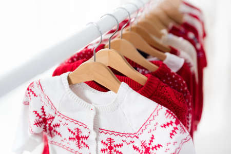 Clothes rack with red Christmas knit wear. Wardrobe with knitted winter jumper and dress. Xmas clothing collection. Christmas gifts shopping. Winter sale for children wear. Kids clothing shop.の写真素材