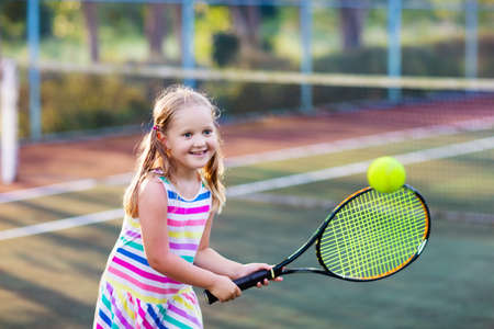Child playing tennis on outdoor court. Little girl with tennis racket and ball in sport club. Active exercise for kids. Summer activities for children. Training for young kid. Child learning to play.の写真素材