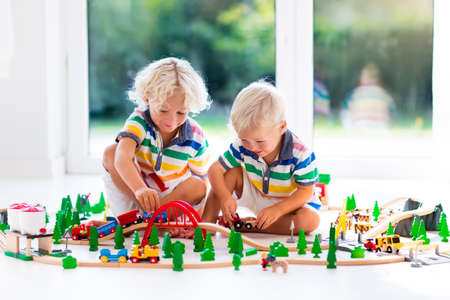 Kids play with toy train railway. Children playing with wooden trains. Toys for little boy. Two brothers build rail road and blocks at home or daycare, preschool. Kindergarten educational games.の写真素材